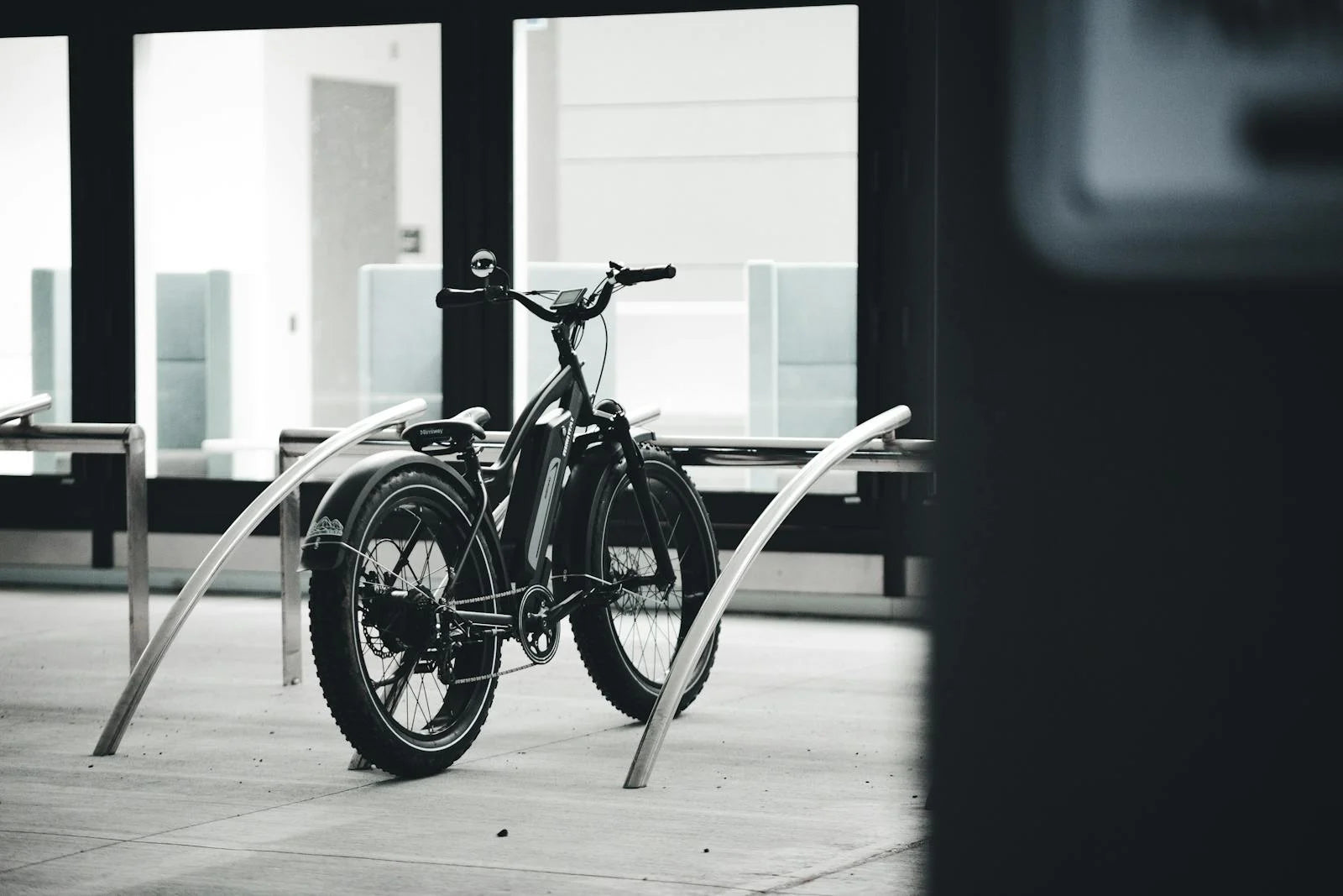 SalteBikes Fat Tire Electric Cruiser Bike – Black e-bike parked at a modern urban rack, ideal for city commutes, off-road trails, and everyday adventures. Shop fat tire e-bikes at SalteBikes.